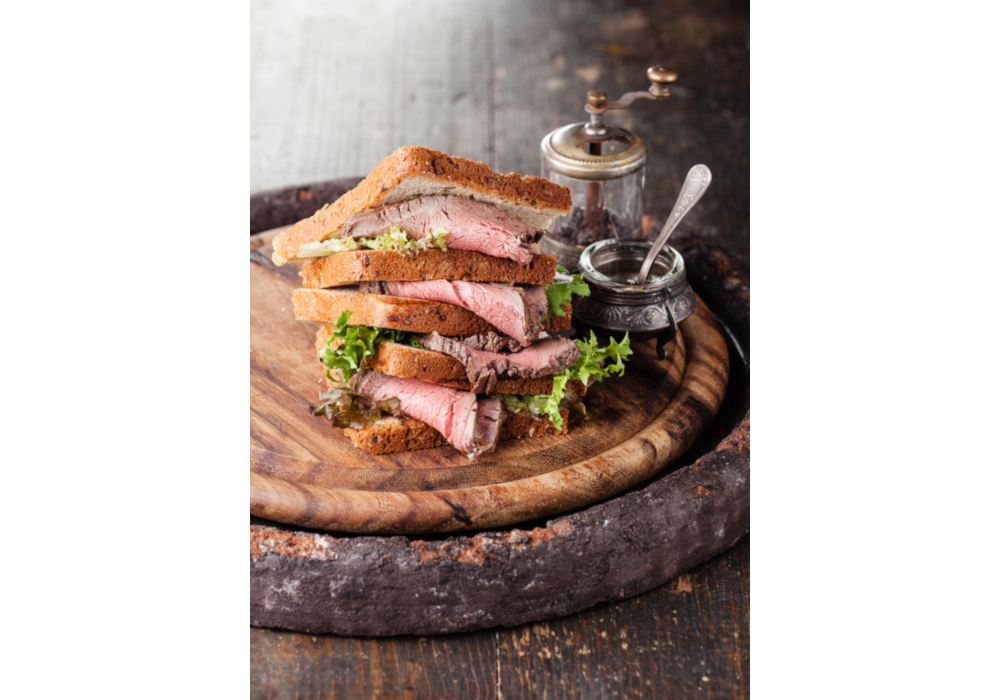 Sandwich mit dünnem Roastbeef und Salat auf einem Holzbrett
