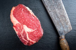 Dry Aged Entrecote Steak auf einer schwarzen Platte und einem Beil daneben