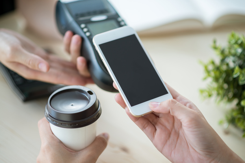 Kunde bezahlt kontaktlos mit dem Smartphone und in der anderen Hand ein Kaffee