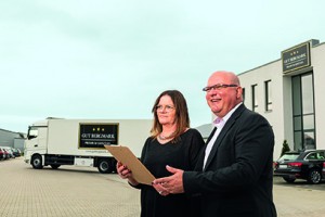 Ein Mann und eine Frau vor einen LKW und einem Bürogebäude mit einem Klemmbrett